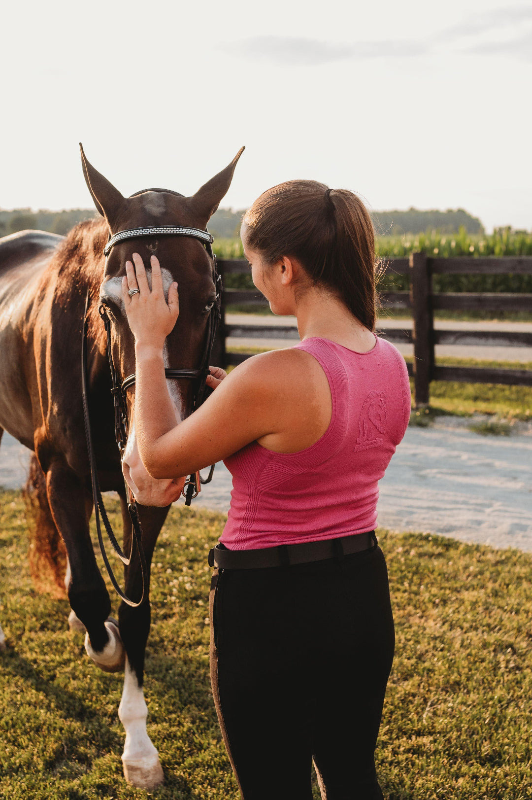 Woman in a pink shirt petting a horse in a grassy field.
